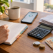 Pessoa organizando finanças pessoais com caderno, calculadora, celular e dinheiro sobre a mesa